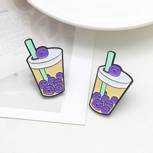 Cute boba milk tea enamel pin with smiling face and green straw on a white desk