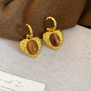 Macro detail of heart-shaped gold earring with tiger eye stone and crystal accent