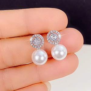 Macro shot of silver pearl earrings featuring pavé cubic zirconia and a center sparkling diamond