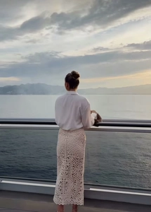 Femme élégante en chemisier blanc et jupe en dentelle ajourée face à la mer au coucher du soleil
