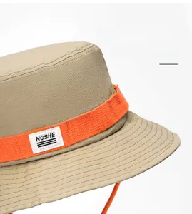 Detailed close-up of khaki bucket hat with orange ribbon and NGSHE woven label