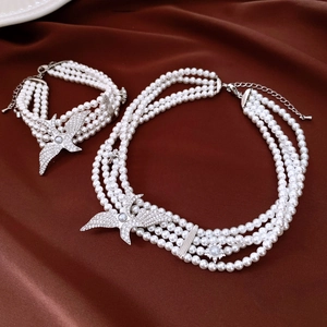 Detailed view of multilayer pearl necklace and bracelet set with eagle charms on red silk
