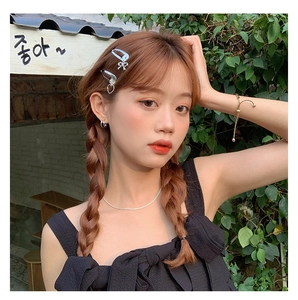 Close-up of a silver bow hair clip and heart pendant on a model in a bright outdoor garden