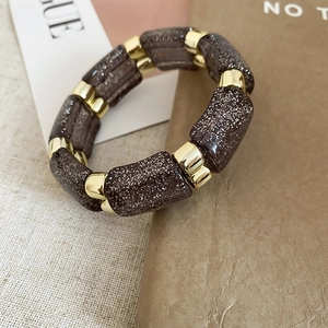 Detailed shot of dark brown resin beads with gold glitter and metallic spacers on a card