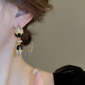Close-up of vintage gold teardrop earrings with black enamel and zircon on ear lobe