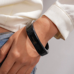 Glossy black resin chunky bangle bracelet shown being worn on a fashion model's wrist.