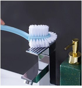 Detail of blue multi-functional cleaning brush with white bristles scrubbing a metal faucet