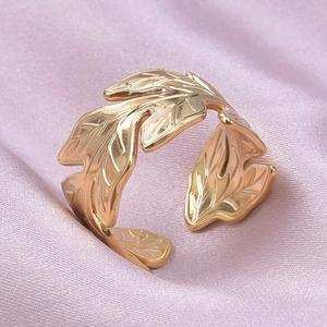 Macro detail of golden leaf-shaped adjustable ring on soft pink silk fabric background