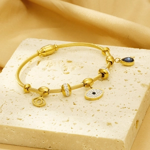 Macro view of golden cable bangle featuring blue gemstone and crystal evil eye charms