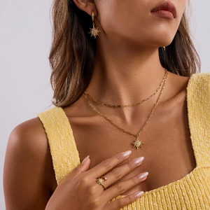 Nahaufnahme eines goldenen Sonnenschmuck-Sets mit Halskette, Ohrringen und Ring am Modell