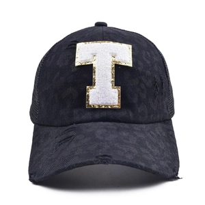 Detail of black trucker hat featuring plush letter T with gold sequins and distressed mesh