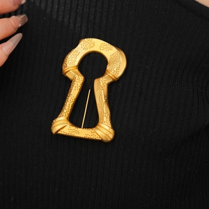 Detail of vintage golden keyhole brooch with matte texture on black knitwear