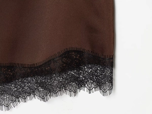 Dettaglio di gonna in raso marrone con bordo in pizzo nero delicato sull'orlo