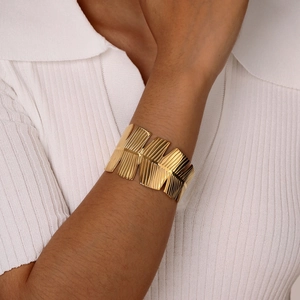 Close-up of golden wide textured metal bangle on model wearing a white ribbed polo shirt