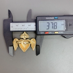 Caliper measuring the 37.8mm width of the gold heart wing ring with red enamel