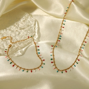 Detail of gold tassel necklace and anklet set with colorful enamel beads on silk background