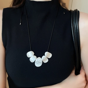 Detailed view of irregular white pendants on a black cord necklace worn on a black turtleneck