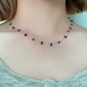 Close-up of fine silver chain with irregular burgundy natural stones on a model