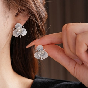 Macro detail of silver flower stud earring featuring a central pearl and zircon petals