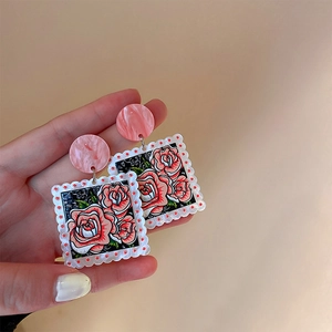 Détail de boucles d'oreilles carrées en acrylique avec roses et bords blancs ondulés