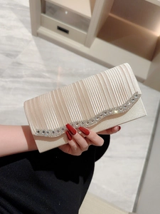 Elegante bolso de noche plisado beige con adornos de strass sostenido a mano en entorno de lujo