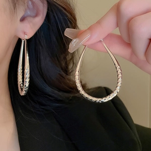 Detail showing large silver teardrop earrings with geometric diamond-cut faceted texture