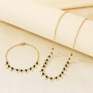Detail of gold chain necklace and bracelet set with black beads and drop pendants