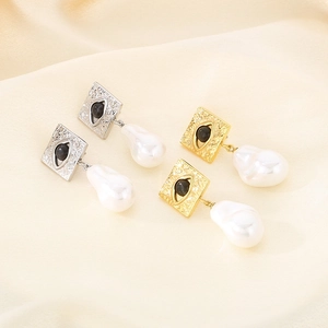Gold and silver Evil Eye square stud earrings with baroque pearl drops on beige background