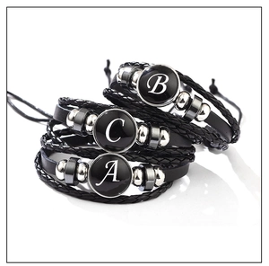 Detailed macro view of woven black leather bracelets with letters A, B, and C charms