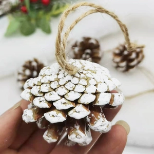 Close-up of a hand holding a natural pinecone ornament with white painted snow and hemp rope