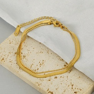 Close-up of dual-layer gold snake chain and bead anklet on a minimalist stone display