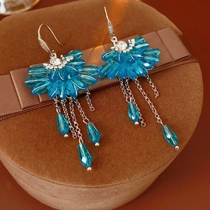 Détail de boucles d'oreilles fleurs bleues à pompons argentés sur un coffret en velours