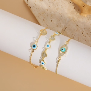Three gold evil eye bracelets with crystal hearts and letter A charms on white props