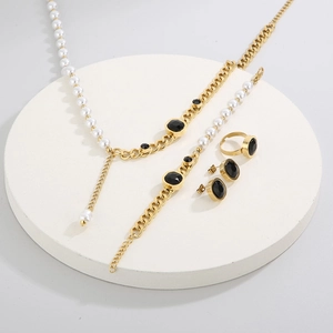 Close-up of golden jewelry set with black round stones and pearls on white base