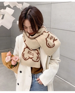 Detail view of beige knit scarf featuring brown bear patterns and soft textured fabric