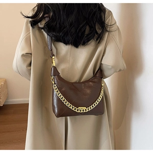 Detail of dark brown quilted leather bag with gold chain strap worn with a beige trench coat