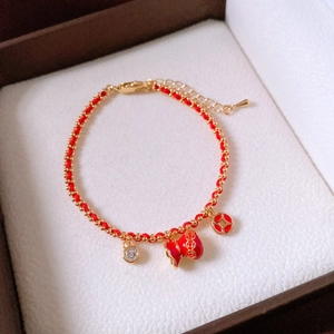 Detailed close-up of a red rope bracelet with 18k gold plated lucky bag and zircon charms