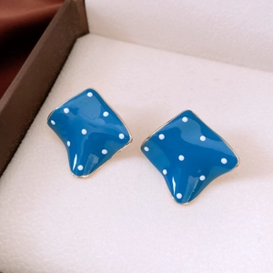 Detailed close-up of blue and white polka dot square earrings in a beige velvet jewelry box