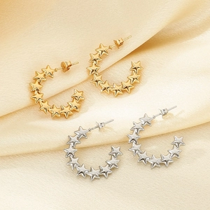 Detailed view of gold and silver stainless steel star earrings on soft silk fabric