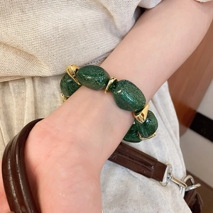 Close-up of green resin beads and gold horseshoe links on a chunky chain bracelet