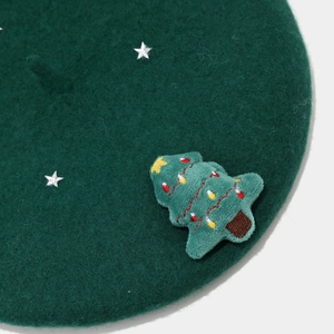 Detail of dark green wool beret featuring silver stars and plush Christmas tree patch