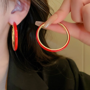 Close-up of a model wearing large red enamel and gold-finish hoop earrings for women
