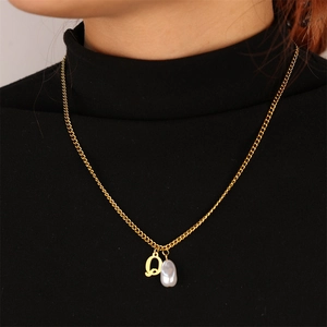Detail of a gold-plated necklace featuring a letter Q pendant and a white baroque pearl