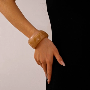 Detail view of a wide amber acrylic marble cuff bracelet worn on a woman's wrist