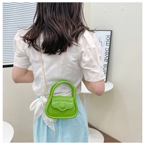 Mini green jelly bag with gold chain and round buckle worn over a model shoulder