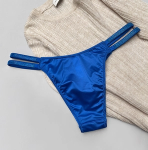 Close-up of blue satin thong with sparkling rhinestone straps on beige knitwear