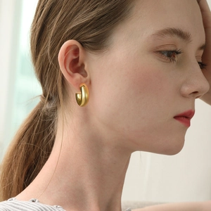 Close-up of a model wearing chunky gold-toned C-shape earrings with a high-polished finish