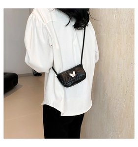 Detail of a black crossbody bag featuring a white butterfly buckle worn by a model