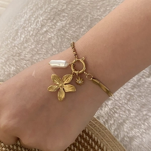 Primo piano di un bracciale dorato con ciondoli a fiore, perla e stella sul polso