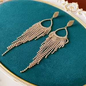 Detailed macro of gold tassel earrings with rhinestones on a green velvet tray